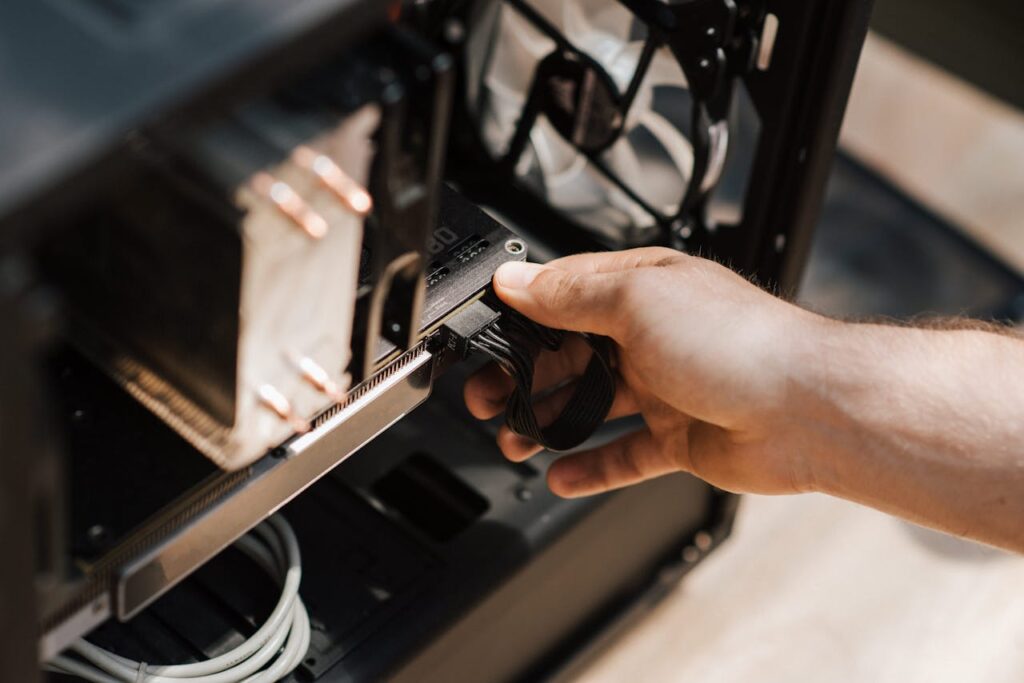 Close-up shot of a hand connecting cables in a computer tower, illustrating tech maintenance.