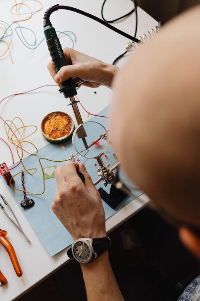 Close-up of a technician repairing a circuit board with a soldering iron and magnifying glass.